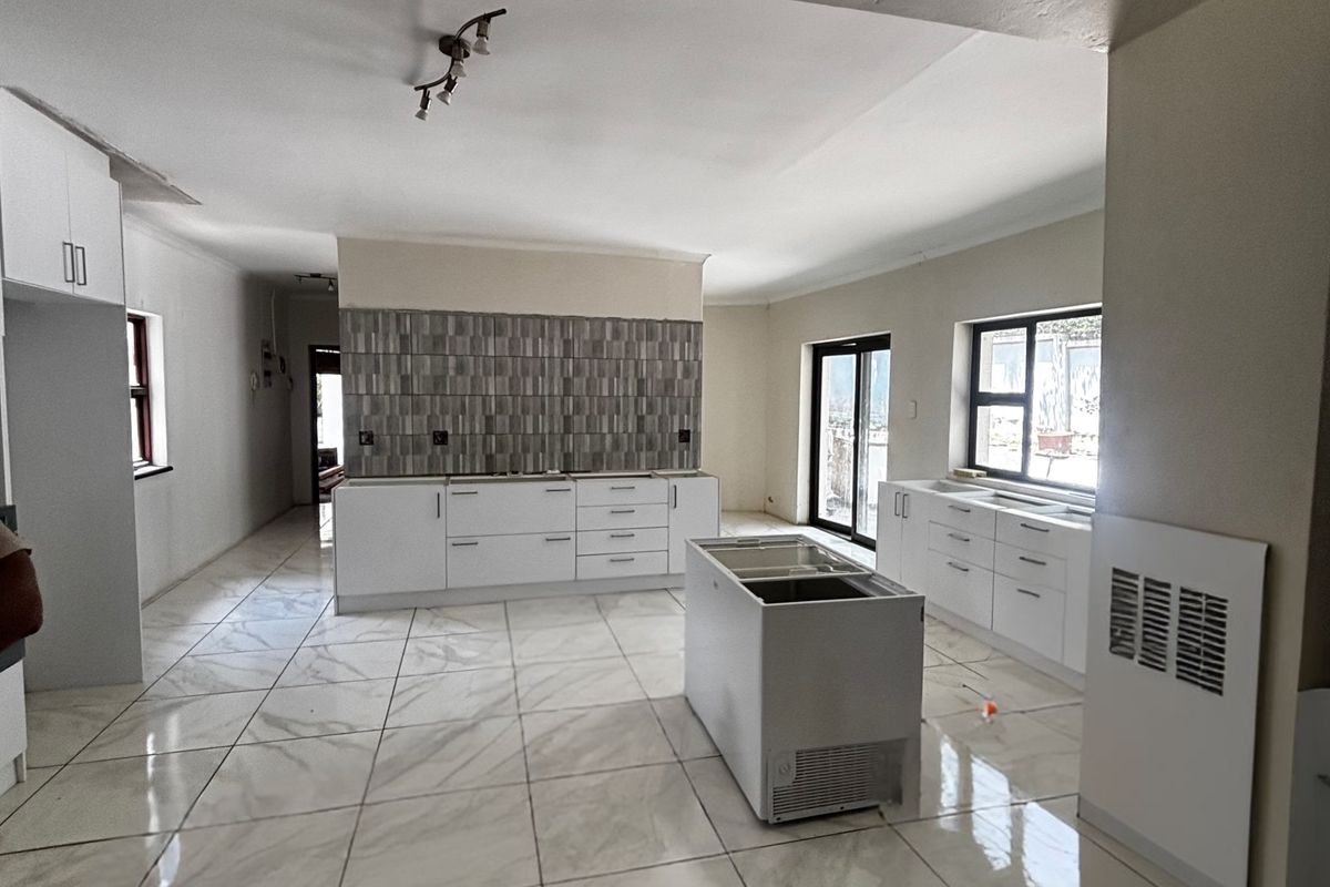 Spacious open-plan kitchen area featuring modern white cabinetry, large format floor tiles, and a central island, currently in an unfinished state.