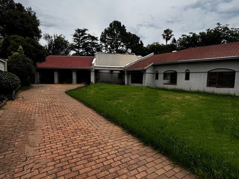 Front view of a single-story house featuring a brick paved driveway, tiled roof, and large lawn area requiring maintenance.