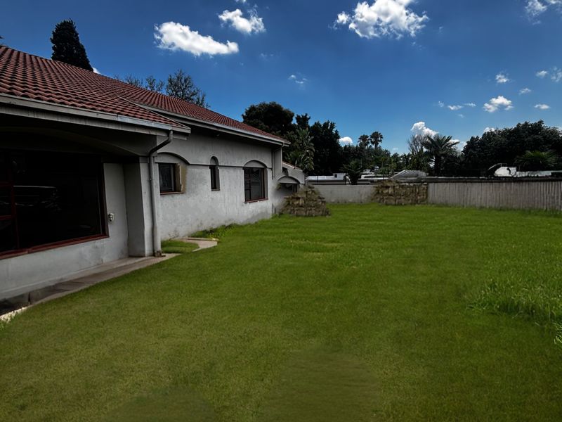 A spacious rear garden featuring a well-maintained lawn, perimeter walling, and a view of the rear elevation of the house with a tiled roof.