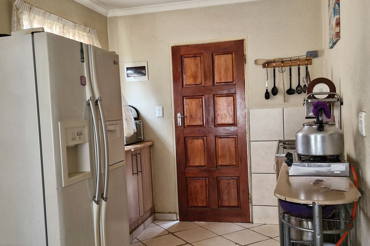 A compact kitchen area featuring tiled flooring, wooden cabinetry, and a solid timber door, showing signs of age and wear.