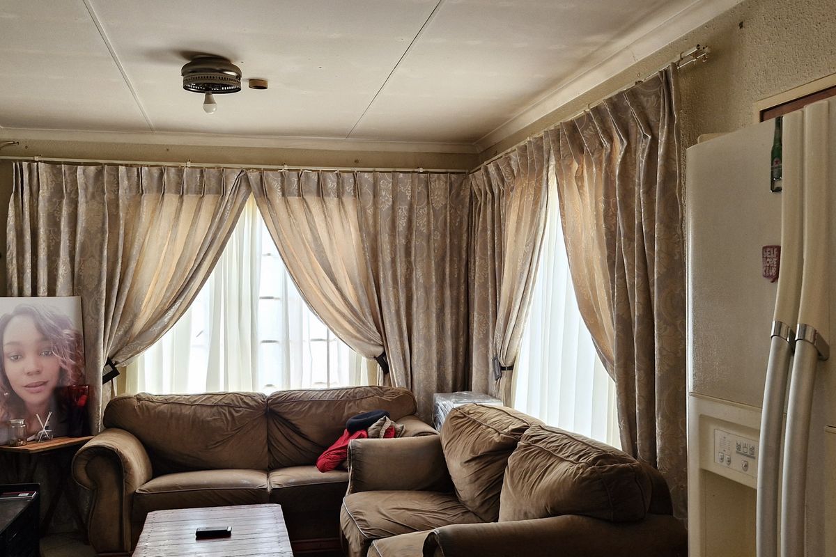 A living room area featuring large windows with floor-to-ceiling curtains, a ceiling-mounted light fixture, and neutral wall finishes.