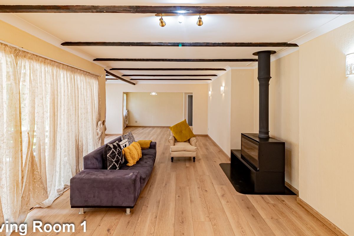 Spacious living room featuring exposed timber ceiling beams, light wood-look flooring, and a modern black freestanding fireplace.