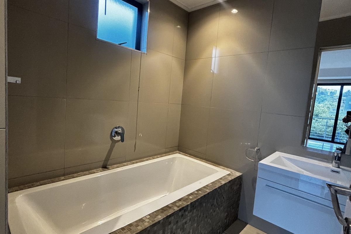 Modern bathroom featuring a built-in bathtub with mosaic tile surround, wall-mounted vanity, and large format neutral wall and floor tiles.