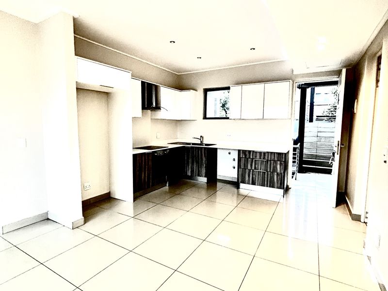 Modern open-plan kitchen featuring sleek cabinetry, integrated hob, extractor fan, and tiled flooring, leading directly to an outdoor patio area.