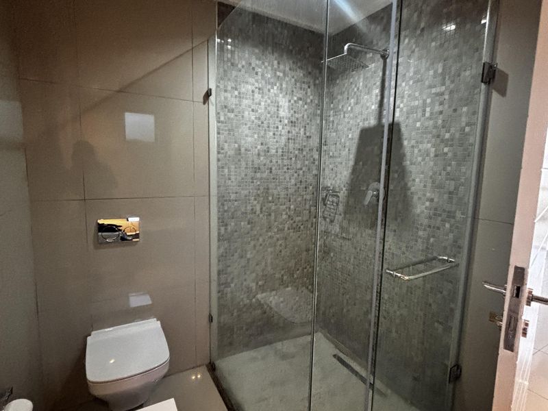 Modern bathroom featuring a glass-enclosed walk-in shower with mosaic tile accents, wall-mounted toilet, and large format floor tiles.