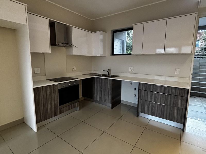Modern kitchen featuring two-tone cabinetry, stone countertops, integrated oven, hob, and extractor fan with tiled flooring and recessed ceiling lighting.