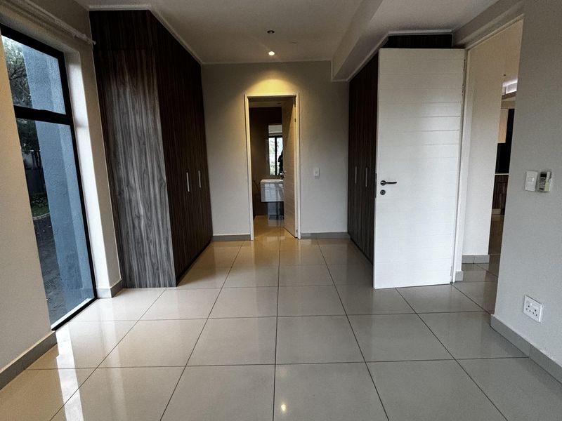 A bright, modern hallway featuring large-format floor tiles, built-in dark wood cabinetry, and recessed ceiling lighting, leading towards an adjacent room.