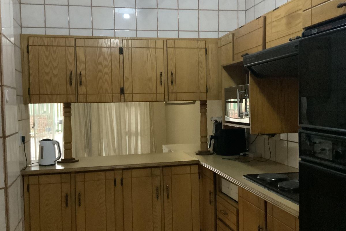 A functional kitchen featuring extensive wooden cabinetry, tiled backsplash, and built-in appliances including an oven, hob, and extractor fan.