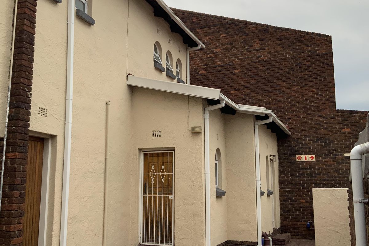 Rear exterior view of the cluster property featuring brick paving, security gates, and arched window detailing along the side facade.