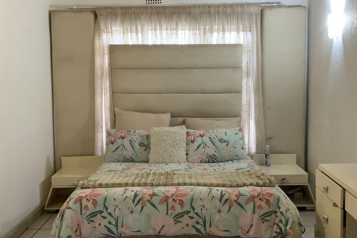 A bedroom featuring a high vaulted ceiling with exposed timber beams, tiled flooring, and a custom built-in headboard with integrated bedside tables.