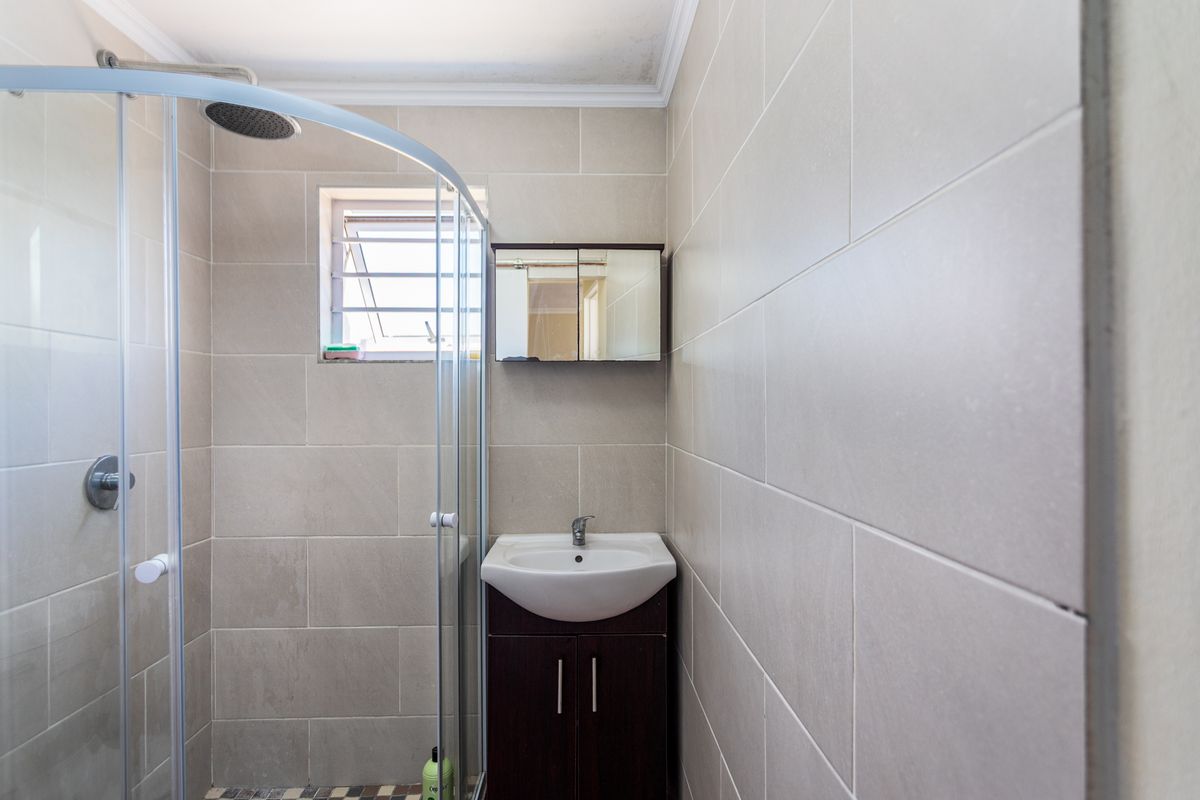 A compact bathroom featuring a glass-enclosed shower, a wall-mounted vanity with a basin, and neutral wall tiling.