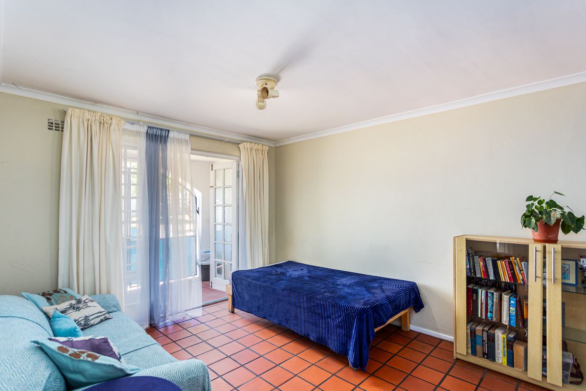 A bedroom featuring terracotta floor tiles and direct access to an outdoor patio through glass-paned double doors.