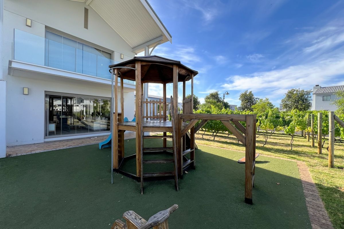 Rear view of the property featuring a modern facade with glass balcony railings, sliding doors, and a landscaped garden area with artificial turf.