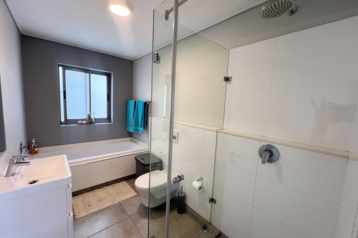 Modern bathroom featuring a glass-enclosed walk-in shower, a built-in bathtub, a vanity basin, and a wall-mounted toilet with contemporary tile finishes.