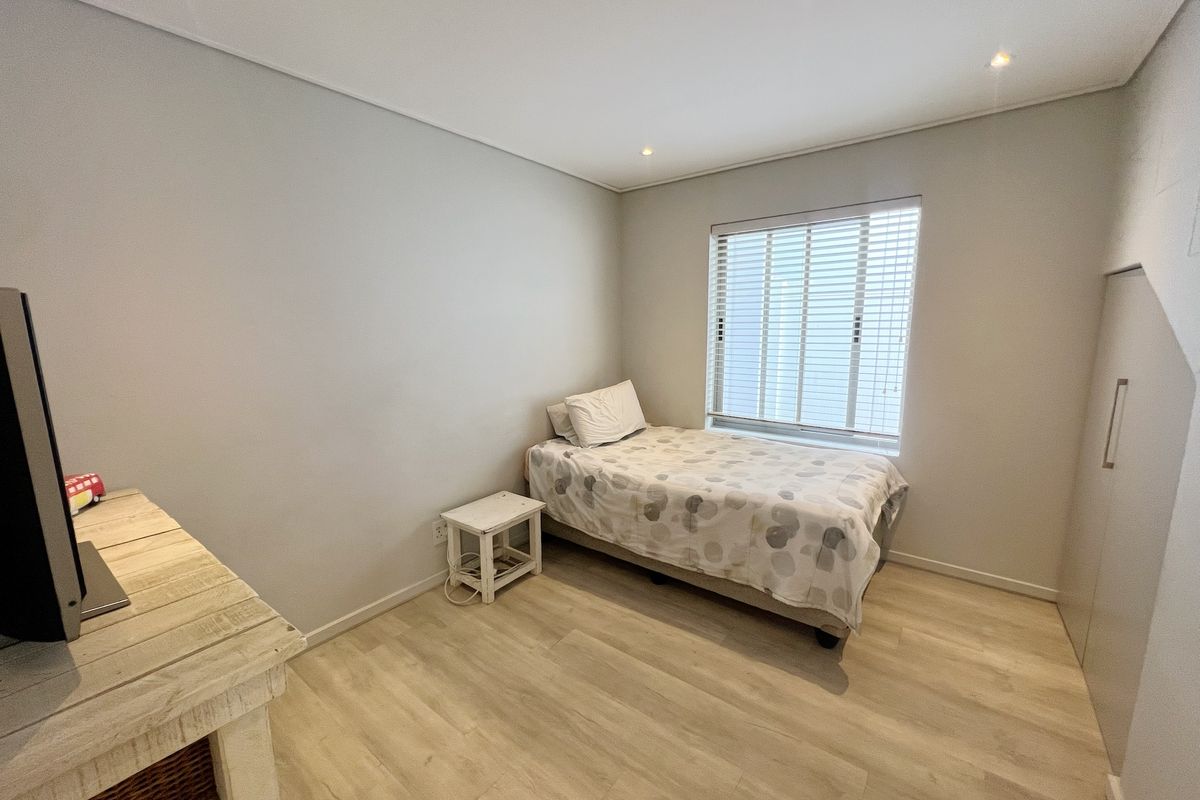 A bright bedroom featuring light wood-look flooring, built-in cabinetry, and a window fitted with horizontal blinds.