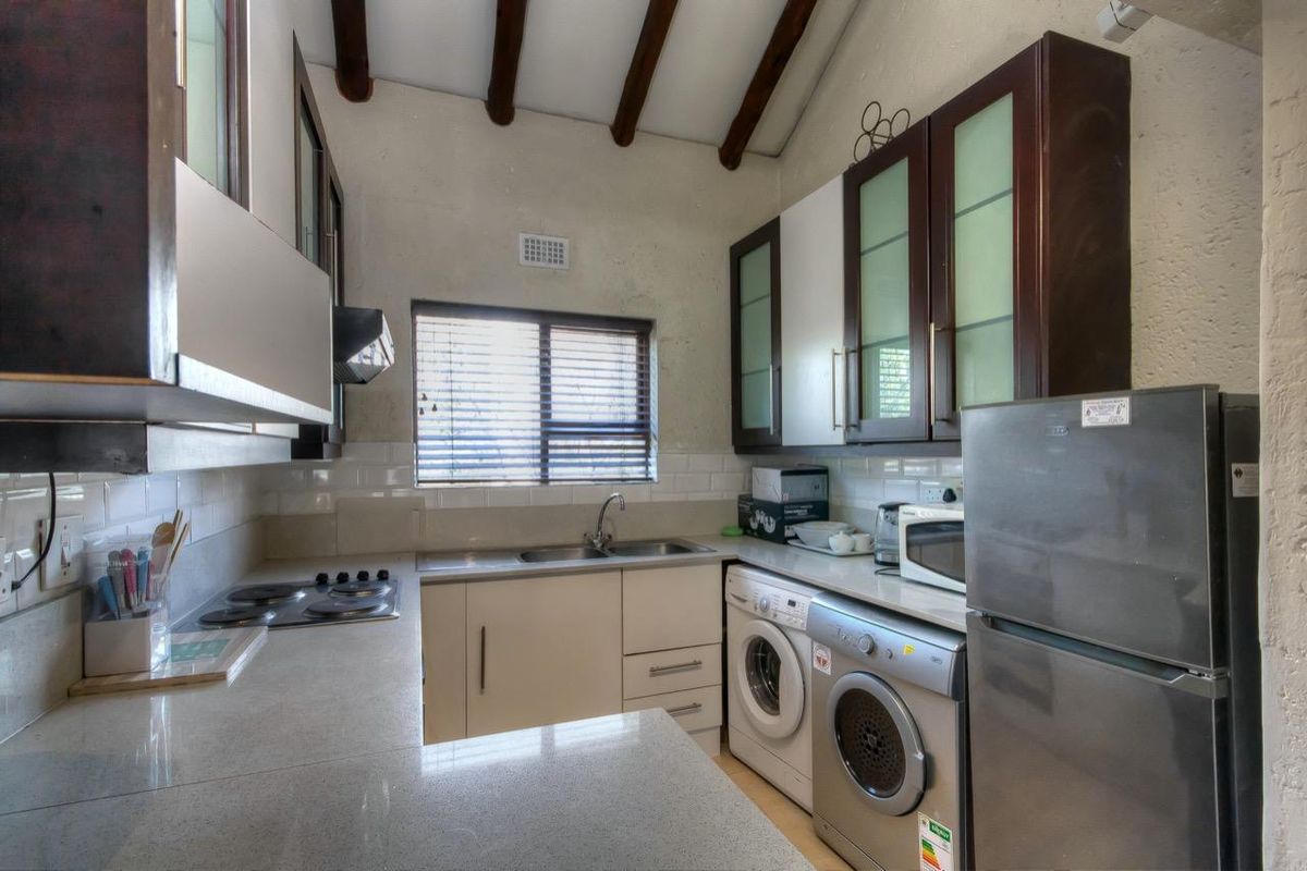 Compact kitchen featuring built-in cabinetry, stone countertops, integrated hob, and dedicated space for laundry appliances under the counter.