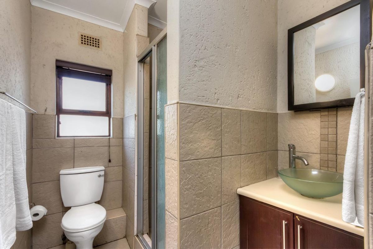 A functional bathroom featuring a glass vessel sink, vanity cabinet, shower enclosure, and toilet with neutral wall and floor tiling.