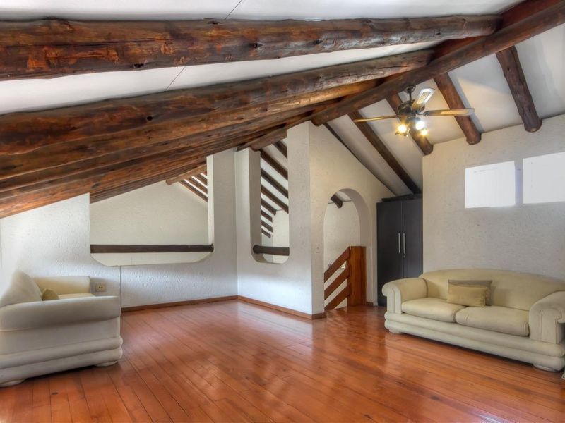 Spacious living area featuring vaulted ceilings with exposed timber beams, polished wooden flooring, and a built-in storage cabinet.