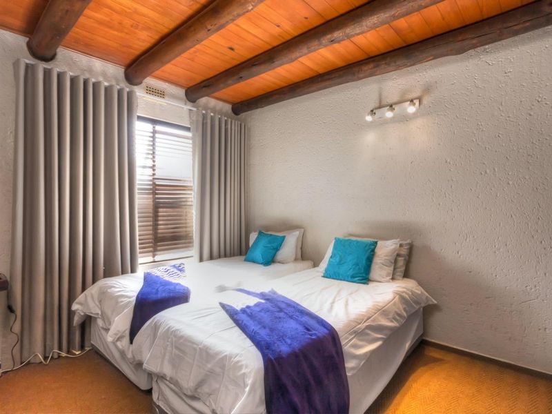 A bedroom featuring exposed timber ceiling beams, textured walls, and built-in wardrobe storage, providing a rustic and cozy atmosphere.