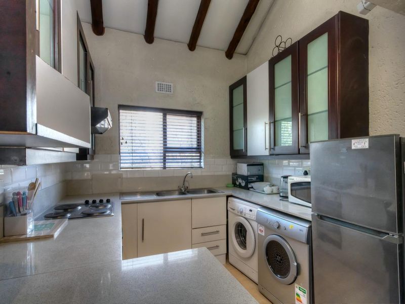 Compact kitchen featuring built-in cabinetry, stone countertops, integrated hob, and dedicated space for laundry appliances under the counter.