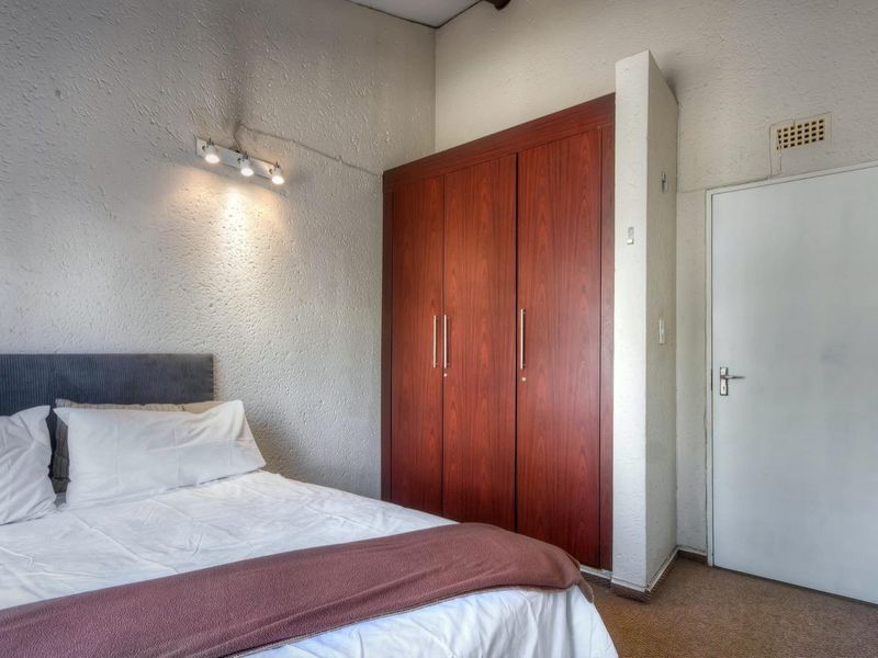 A bedroom featuring built-in wooden cupboards, textured wall finishes, and carpeted flooring, providing functional storage and a neutral living space.