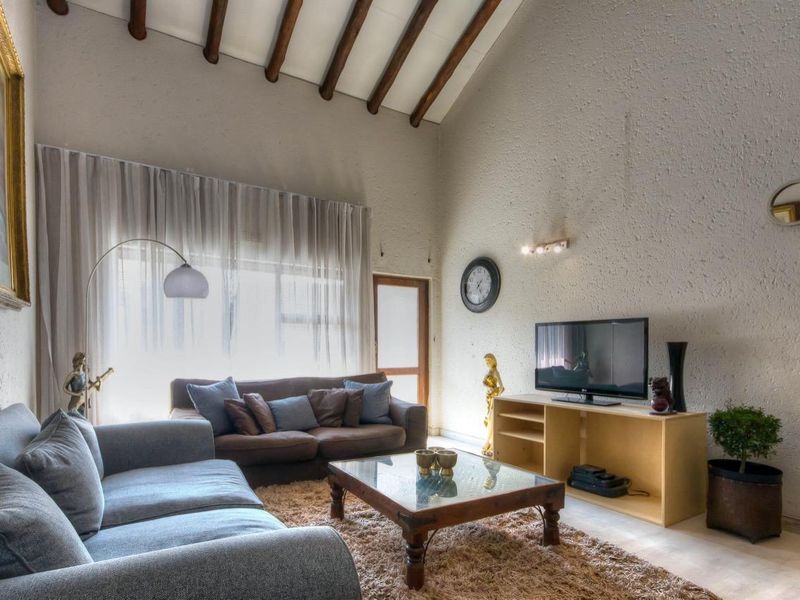 Spacious living room featuring high vaulted ceilings with exposed timber beams, large windows, and textured wall finishes.