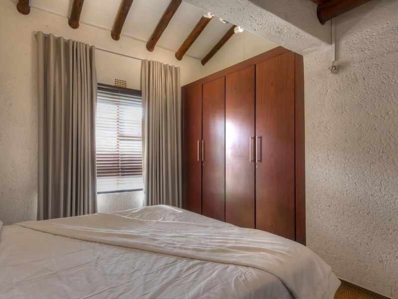A bedroom featuring exposed timber ceiling beams, textured walls, and built-in wooden cabinetry providing ample storage space.