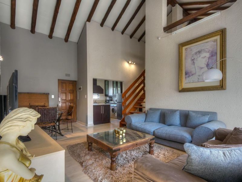 Open-plan living area featuring high vaulted ceilings with exposed timber beams, a mezzanine level, and an adjoining kitchen space with wooden cabinetry.