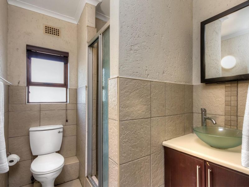A functional bathroom featuring a glass vessel sink, vanity cabinet, shower enclosure, and toilet with neutral wall and floor tiling.