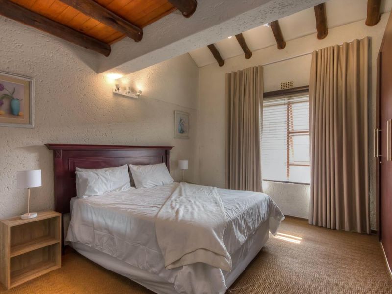 A cozy bedroom featuring exposed timber ceiling beams, textured walls, built-in wardrobes, and large windows with floor-to-ceiling curtains.
