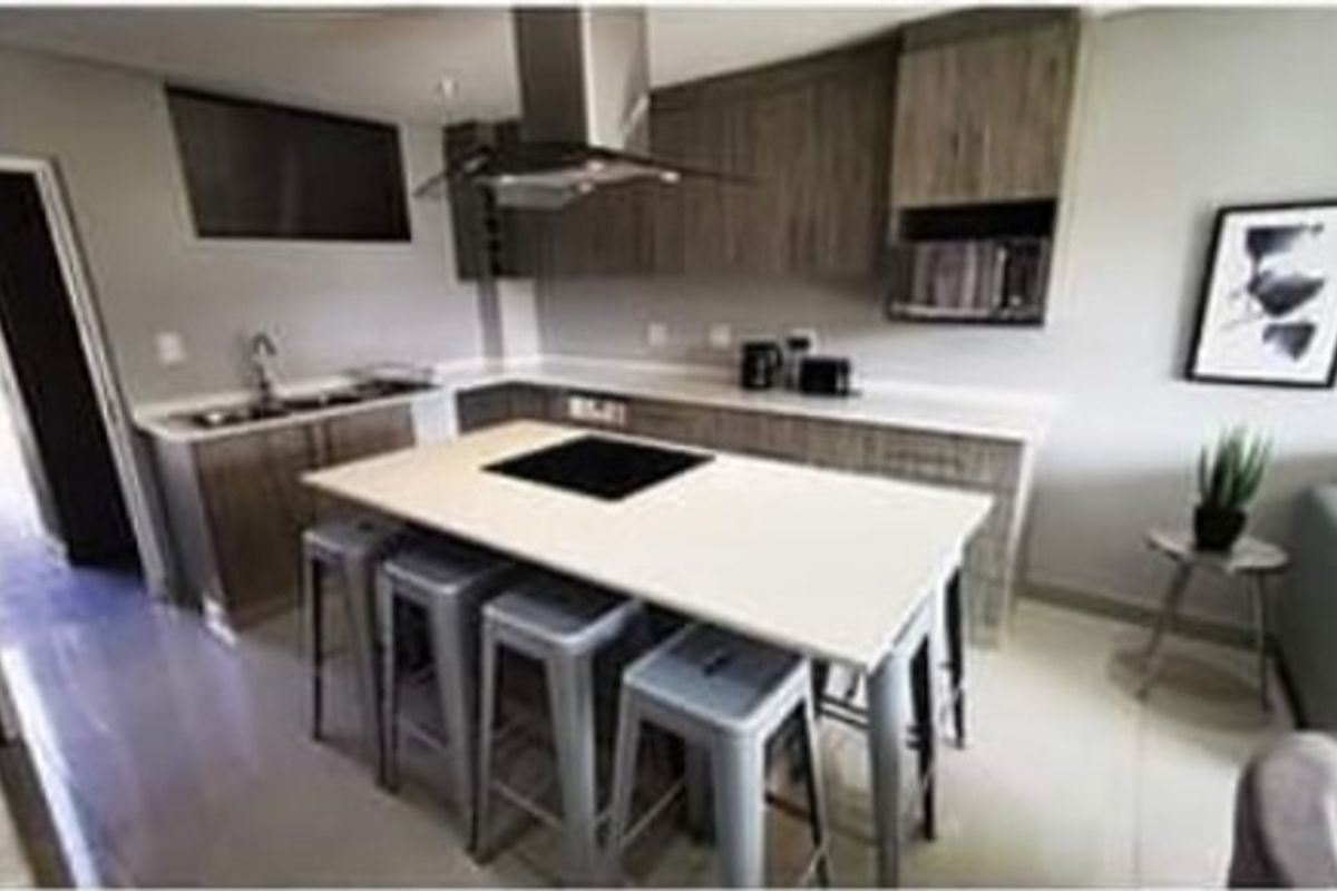 Modern kitchen featuring a central island with a built-in cooktop, sleek cabinetry, stone countertops, and a stainless steel extractor fan.