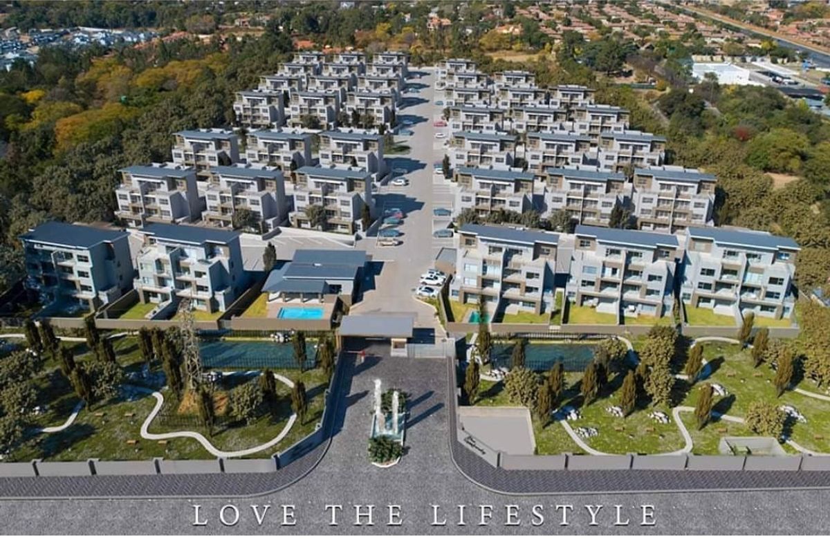 Aerial view of a modern residential apartment complex featuring multiple multi-story buildings, landscaped grounds, swimming pools, and a secure gated entrance.