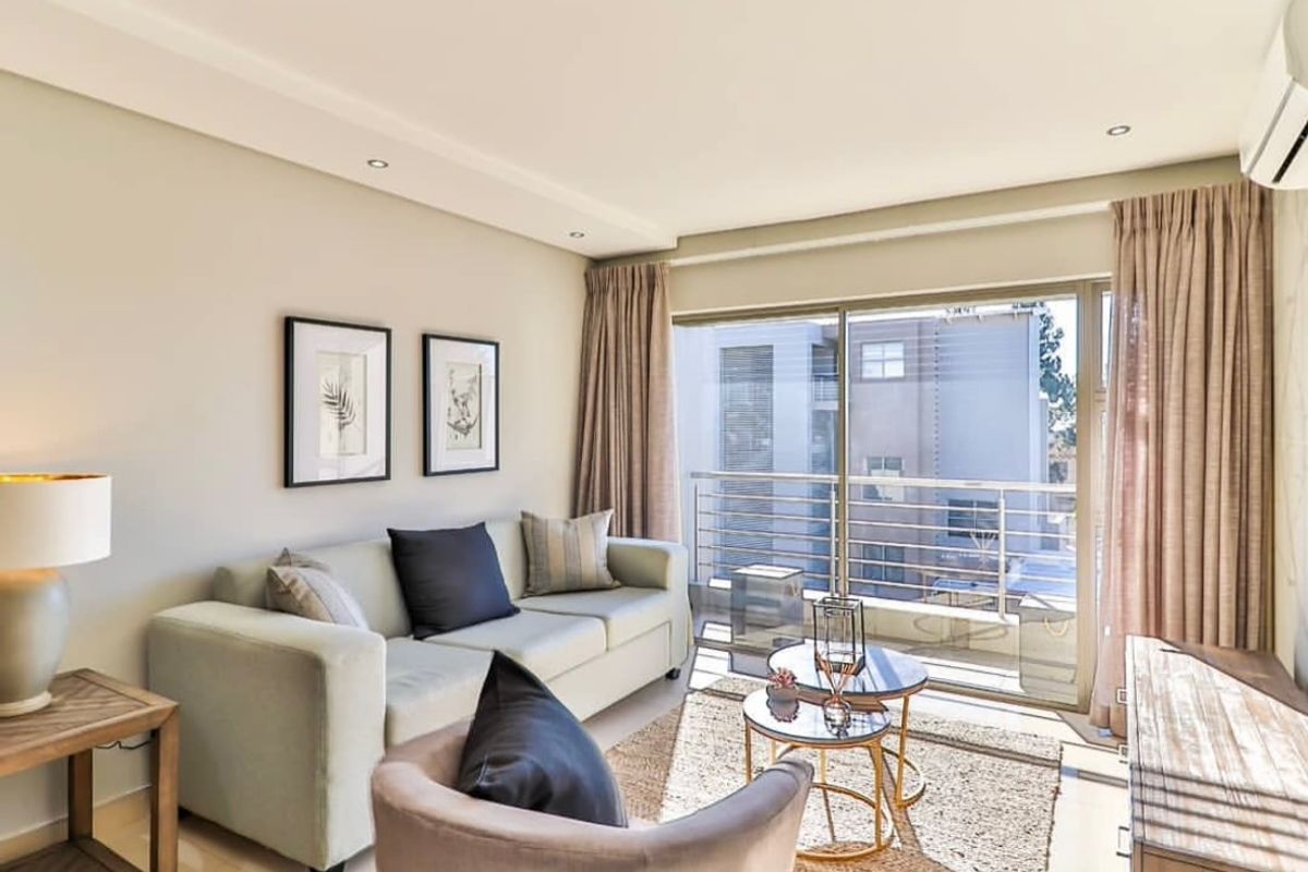 A bright and well-maintained living room featuring recessed ceiling lighting, a wall-mounted air conditioning unit, and large sliding glass doors leading to a balcony.