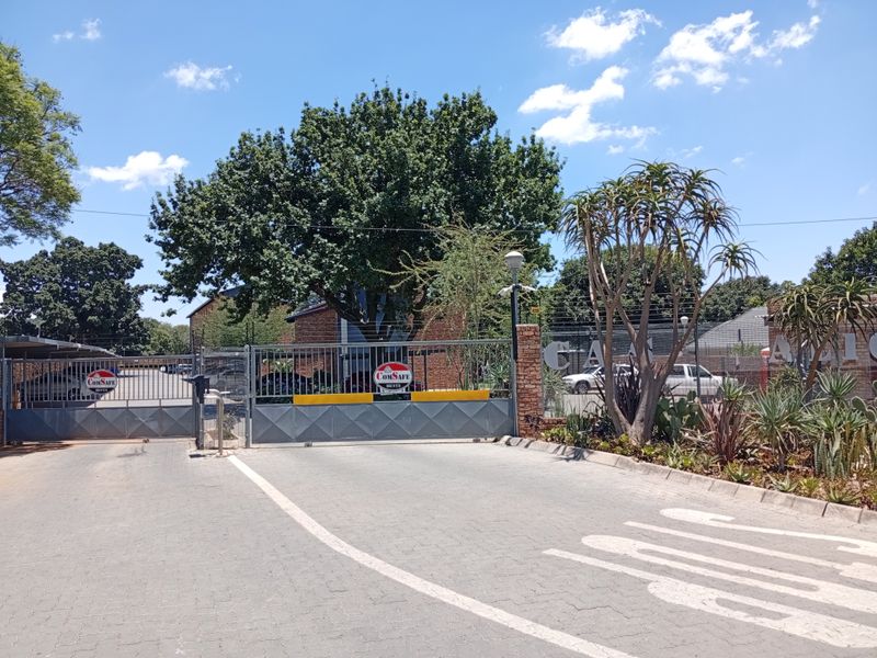 The entrance to the apartment complex features a secure automated gate, electric fencing, and a paved driveway with established landscaping.