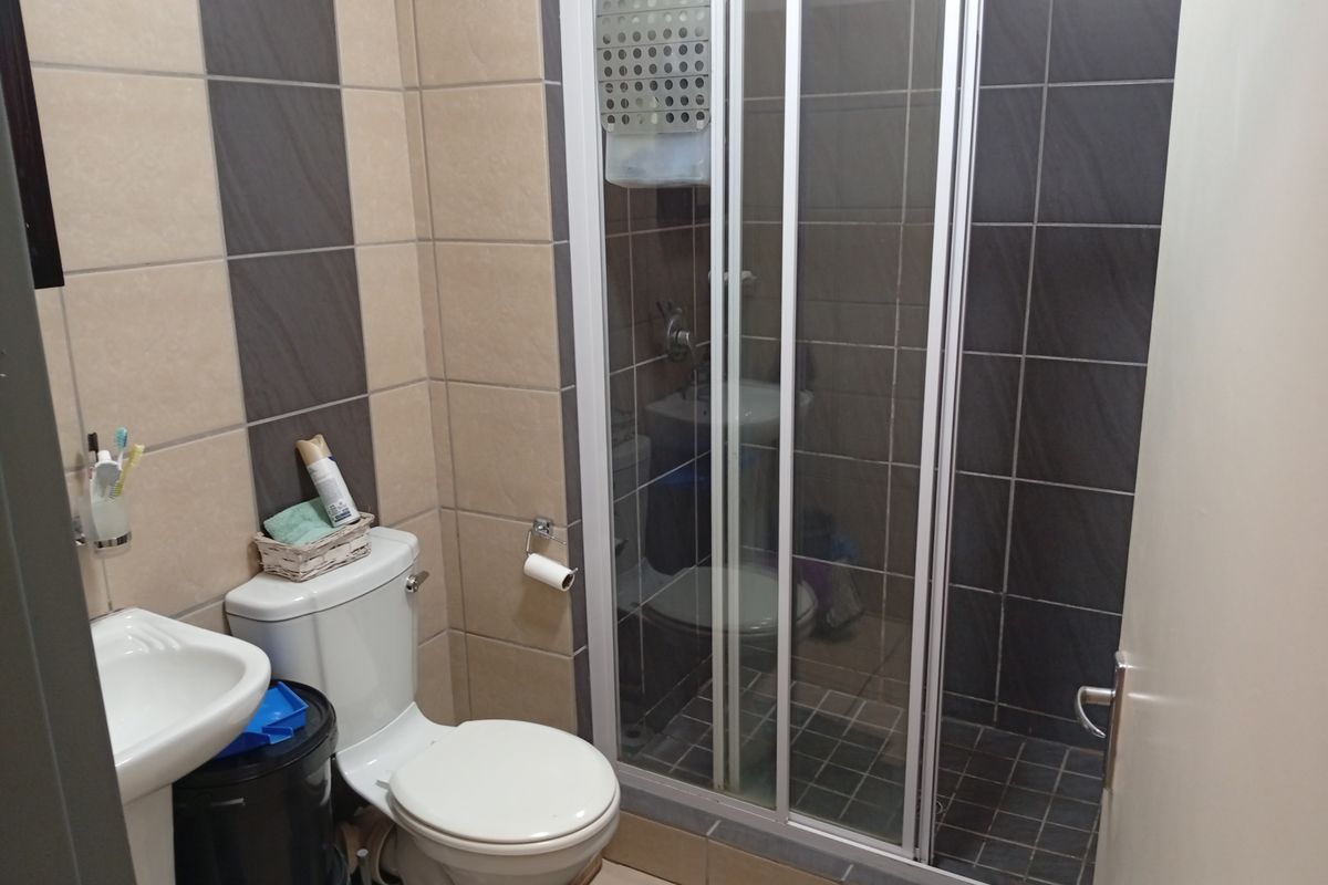 Compact bathroom featuring a pedestal basin, toilet, and a glass-enclosed shower with contrasting beige and dark grey wall tiling.