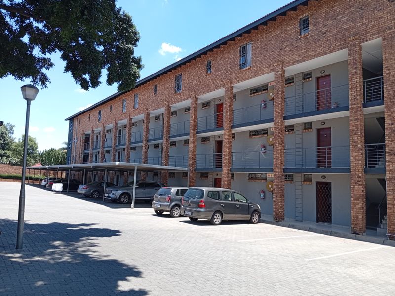 Exterior view of a multi-story apartment complex featuring a brick facade, covered parking bays, and private balconies for each unit.