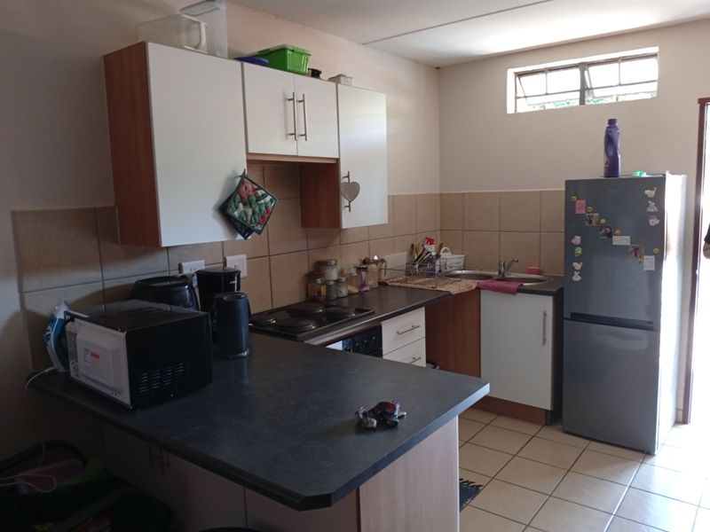 A functional kitchen featuring laminate countertops, built-in cabinetry, an electric hob, and a double sink with tiled backsplash and flooring.