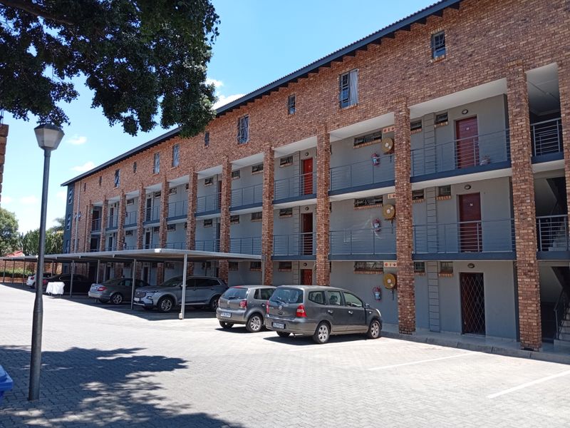 Exterior view of a multi-story apartment complex featuring a brick facade, covered parking bays, and private balconies for each unit.