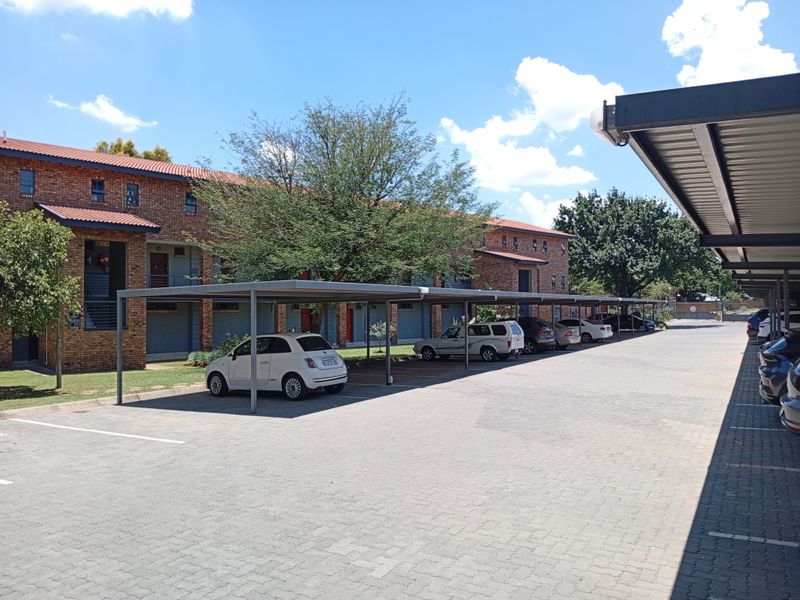 Exterior view of an apartment complex featuring a paved parking area with covered carports and brick building facades.