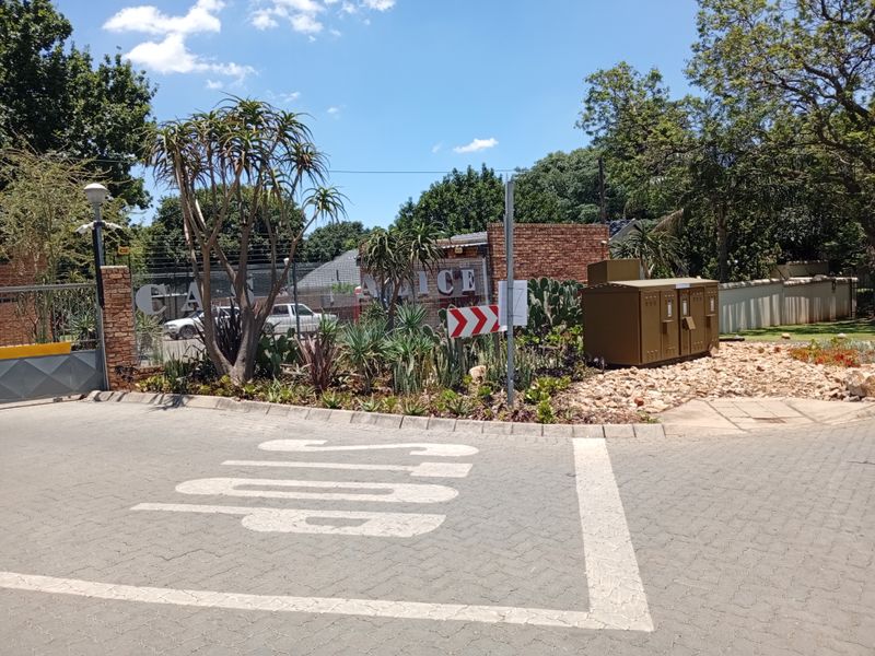 The entrance to the apartment complex features a secure gate, brick boundary wall with electric fencing, and a paved driveway.