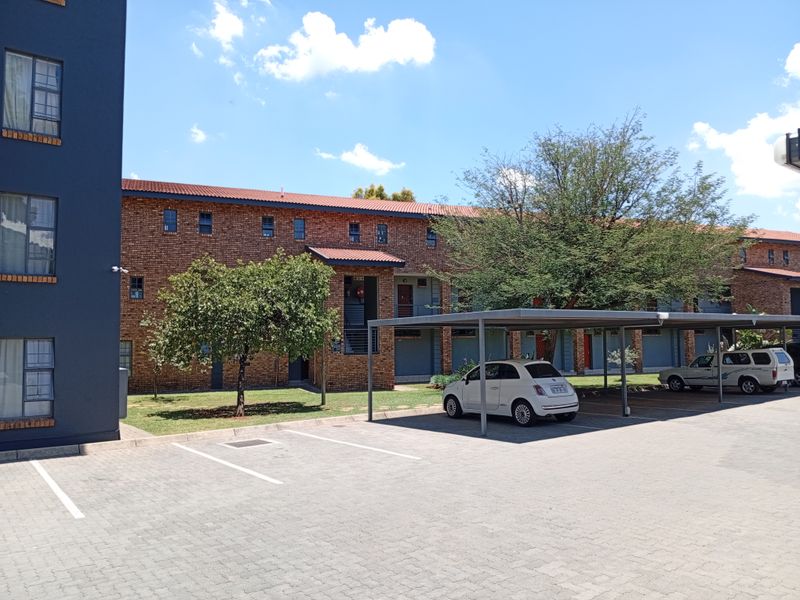 Exterior view of a multi-story brick apartment complex featuring a paved parking area with covered carports and landscaped grounds.