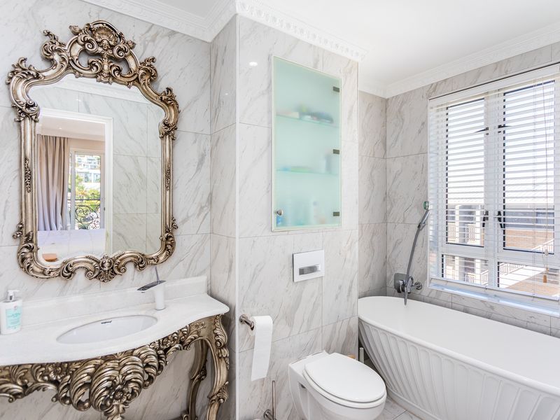 Luxurious bathroom featuring marble-look wall tiles, a sophisticated vanity with an ornate mirror, a wall-mounted toilet, and a modern freestanding bathtub.