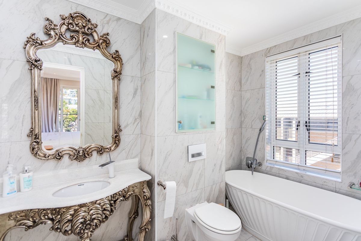 Luxurious bathroom featuring marble-look wall tiles, a sophisticated vanity with an ornate mirror, a wall-mounted toilet, and a modern freestanding bathtub.
