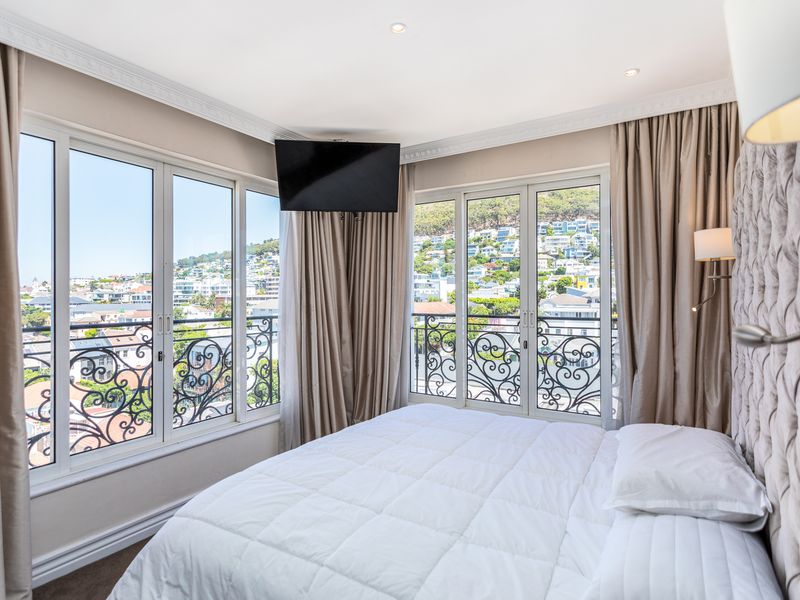 A well-appointed bedroom featuring large windows and glass doors with decorative wrought iron railings, offering expansive views and abundant natural light.