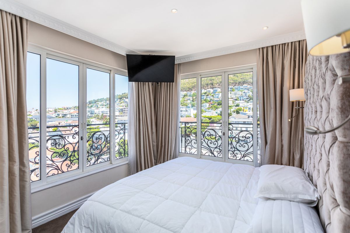 A well-appointed bedroom featuring large windows and glass doors with decorative wrought iron railings, offering expansive views and abundant natural light.