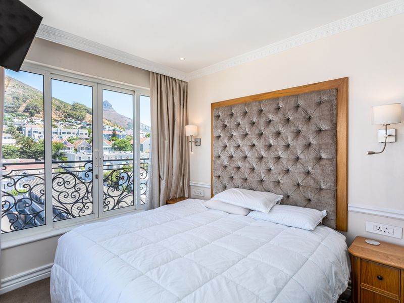 A well-maintained bedroom featuring a tufted headboard, crown molding, and a sliding glass door opening to a balcony with scenic mountain and neighborhood views.