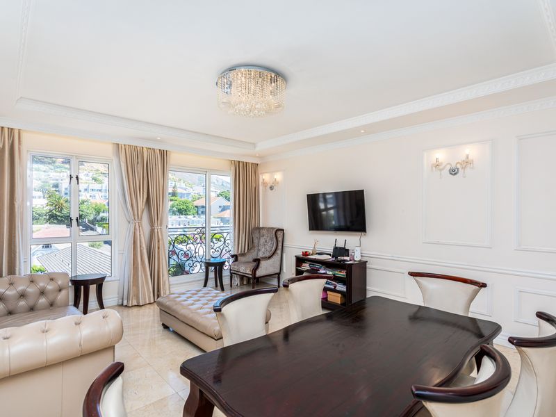 Spacious open-plan living and dining area featuring elegant crown molding, wainscoting, tiled floors, and access to a balcony with scenic views.