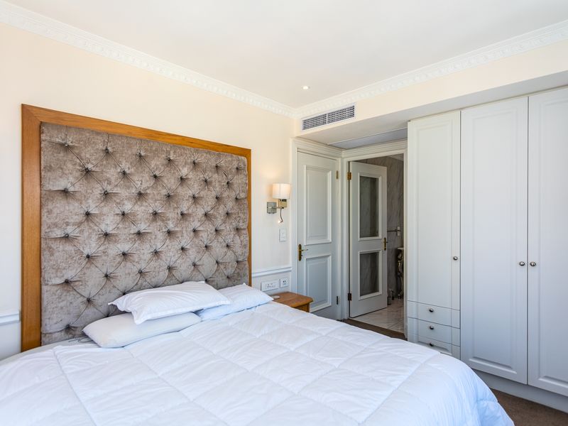 A well-appointed bedroom featuring built-in cabinetry, crown molding, and integrated ducted air conditioning, with an adjoining bathroom visible through the doorway.