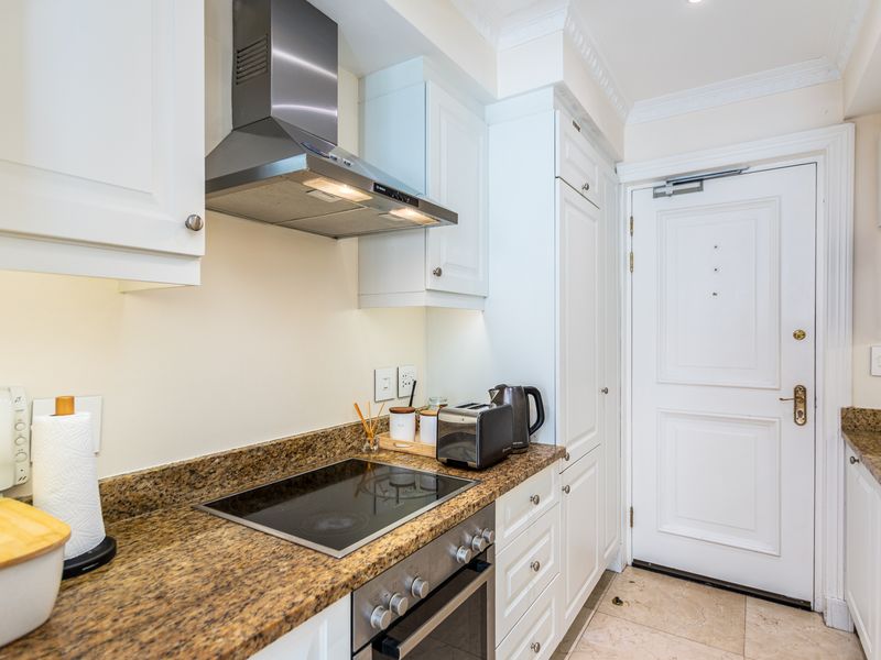 A well-maintained kitchen featuring granite countertops, built-in oven, electric hob, stainless steel extractor fan, and classic white cabinetry with tiled flooring.