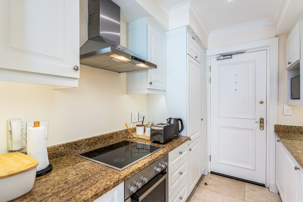 A well-maintained kitchen featuring granite countertops, built-in oven, electric hob, stainless steel extractor fan, and classic white cabinetry with tiled flooring.